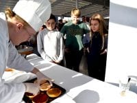 Kokke-elev Mathias Gammelby er i gang med at lave den ”Cheesy American”-burger, der endte med at vinde, mens idémændene bag, Victor, Josefine og Eren, står og kigger på.